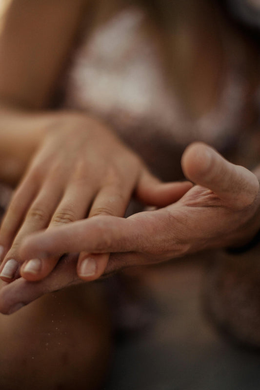 Hand, die von einer anderen Hand behutsam umgriffen wird. Finger sind gestreckt. Hintergrund verschwimmt in umrissen einer Person.